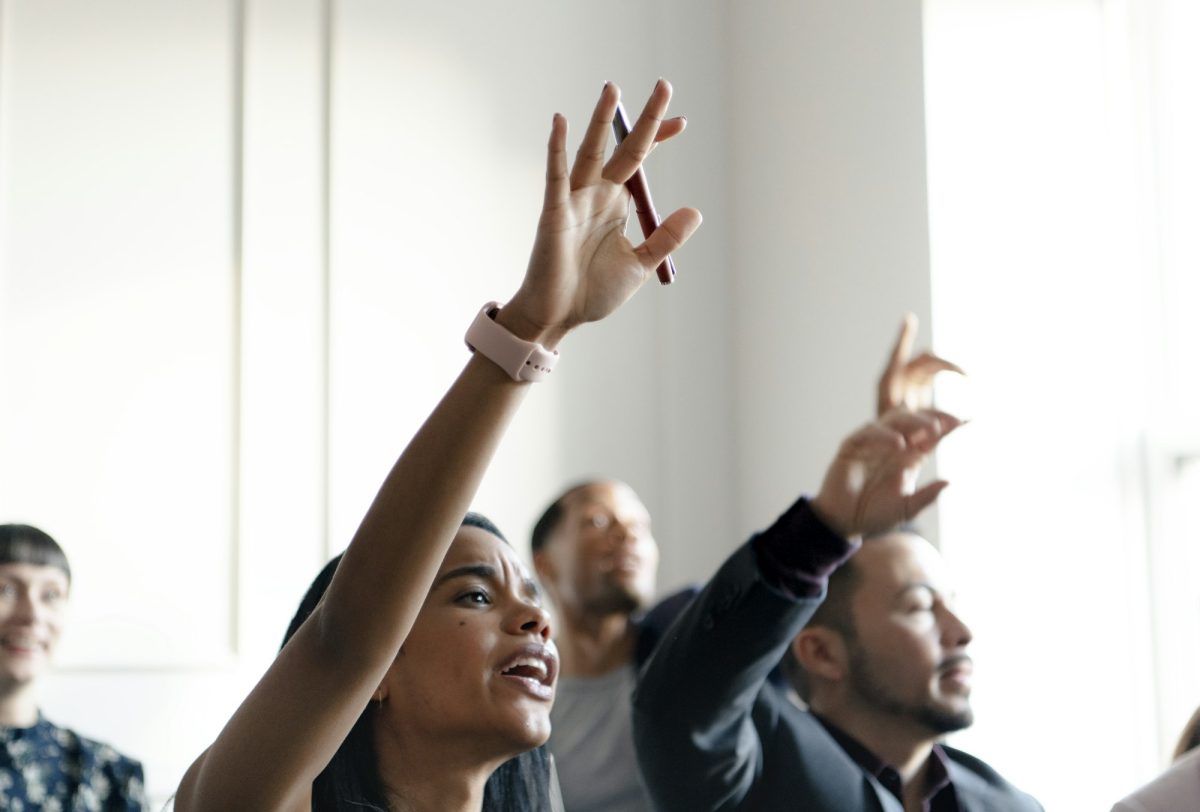 Business people in a seminar raising their hands