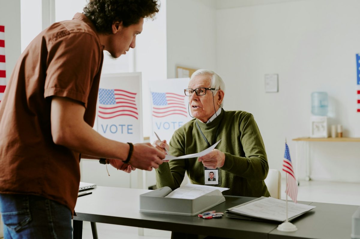 Senior Polling Station Worker Giving Ballot Paper To Young Man